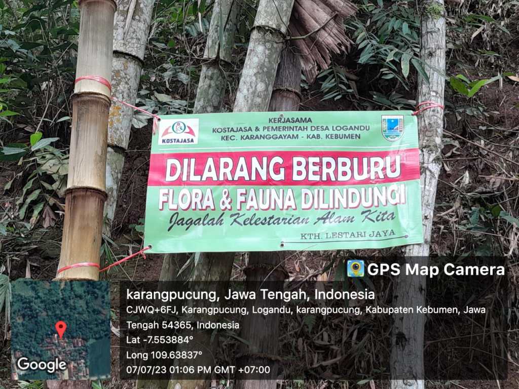A sign in Indonesian stating 'Hunting of Flora & Fauna is Prohibited' in a forested area, emphasizing wildlife protection.